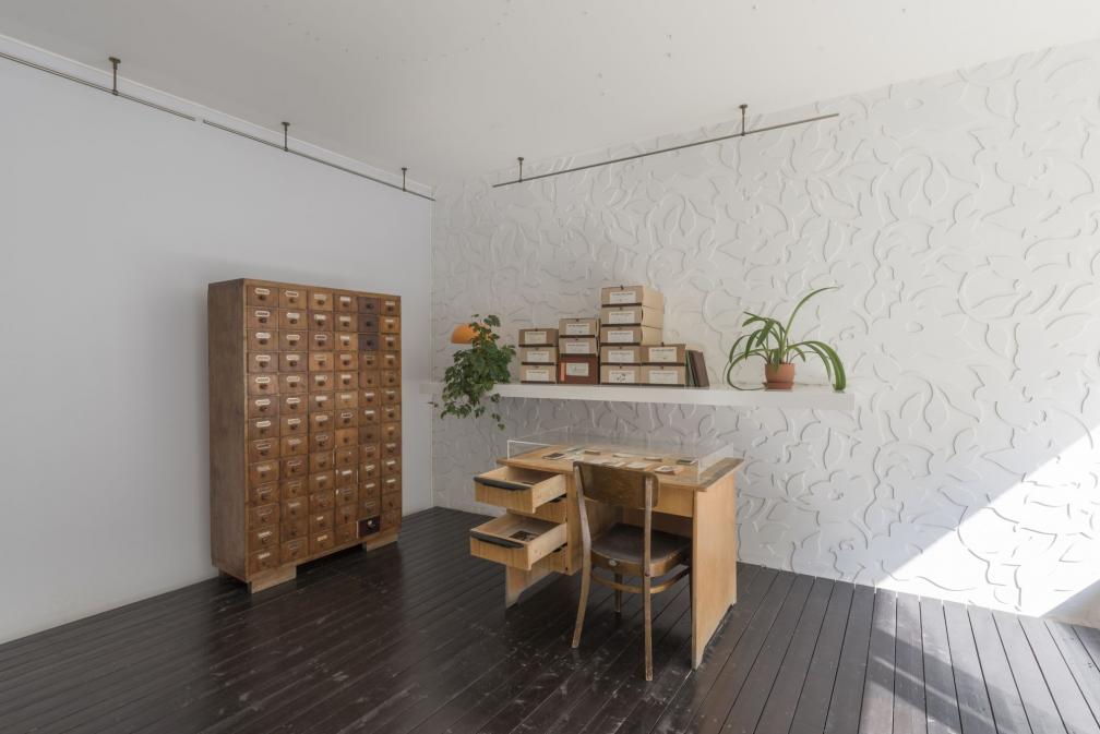 Näituse “Benita Labi: Splendid loneliness” vaade - arhiivikapp, kirjutuslaud, tool ja riiul arhiivikarpidega.